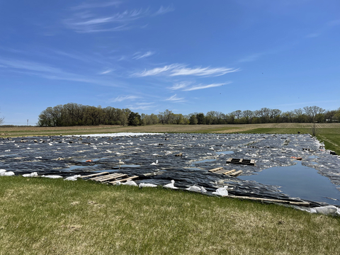 Black silage tarp weighted with sandbags over a grassy field.
